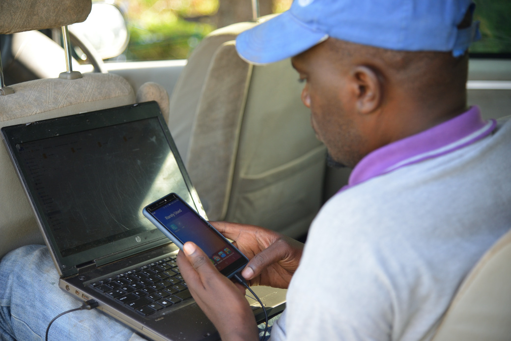 Un homme est assis devant son ordinateur portable et tient un smartphone dans sa main.