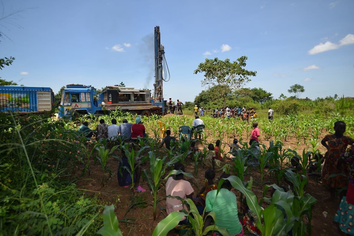 People in a field. In the background a truck with drilling equipment