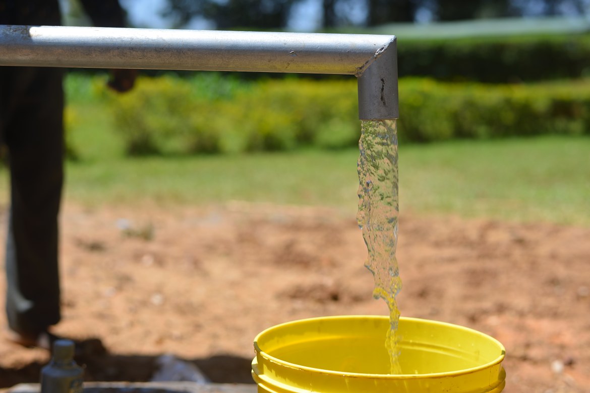 Water flows from a hand pump into a yellow bucket