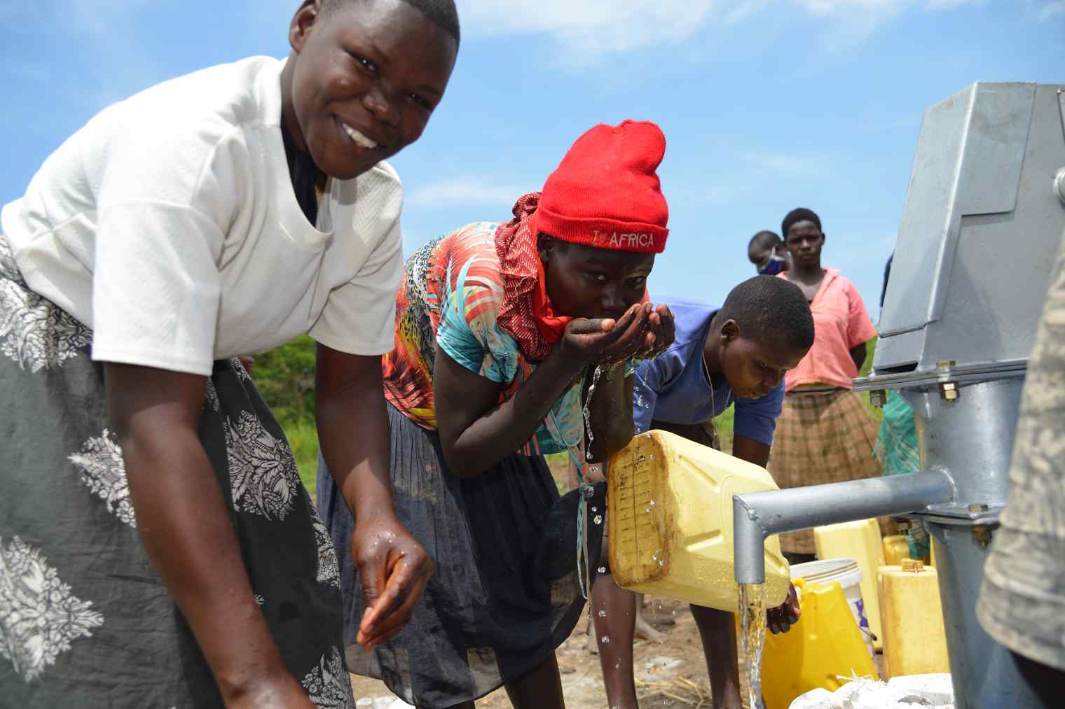 Young African women enjoy the fresh water from a hand pump