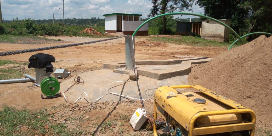 Generator in the foreground. In the background is the borehole with the hose for the pump test.